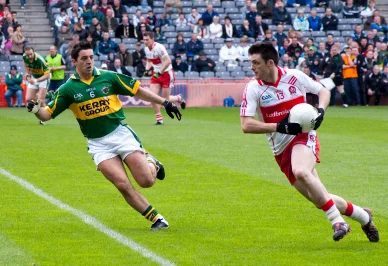 Gaelic football match in progress on an Irish pitch, with players contesting the ball