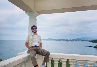 L'acteur Pierre Niney en tenue décontractée, posant sur un balcon avec la mer en arrière-plan.
