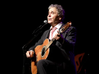 Pierre Perret sur scène avec sa guitare. Pierre Perret avec sa guitare en concert.
