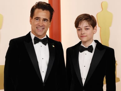 Colin Farrell standing with his son, both dressed casually and smiling at the camera.​