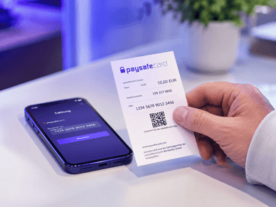 Χέρι κρατά κουπόνι Paysafecard δίπλα σε κινητό Κουπόνι Paysafecard για online αγορές