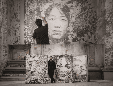 Vhils está ao lado de retratos de grandes dimensões e cria uma obra de parede no estúdio
