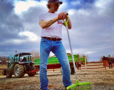 Ett arbetsögonblick ur livet, publicerat av Mikael Persbrandt Mikael Persbrandt i vit T-shirt och keps håller en spade mot en molnig himmel; foto publicerat på skådespelarens officiella konto @mikaelpersbrandtofficial