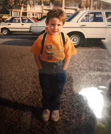 DJ Snake : Les débuts d'une star en herbe. DJ Snake enfant avec un sourire devant des voitures sur une rue animée.