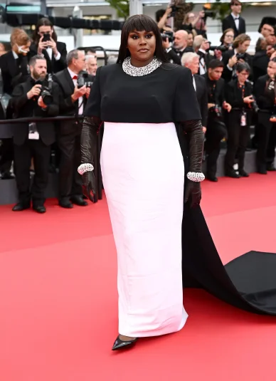 Yseult sur le tapis rouge, vêtue d'une robe bicolore noir et blanc avec des gants en cuir, ornée de bijoux éclatants, entourée de photographes.